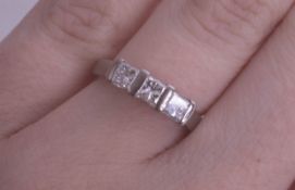 An 18ct white gold and three stone diamond ring set with princess cut diamonds, size I.
