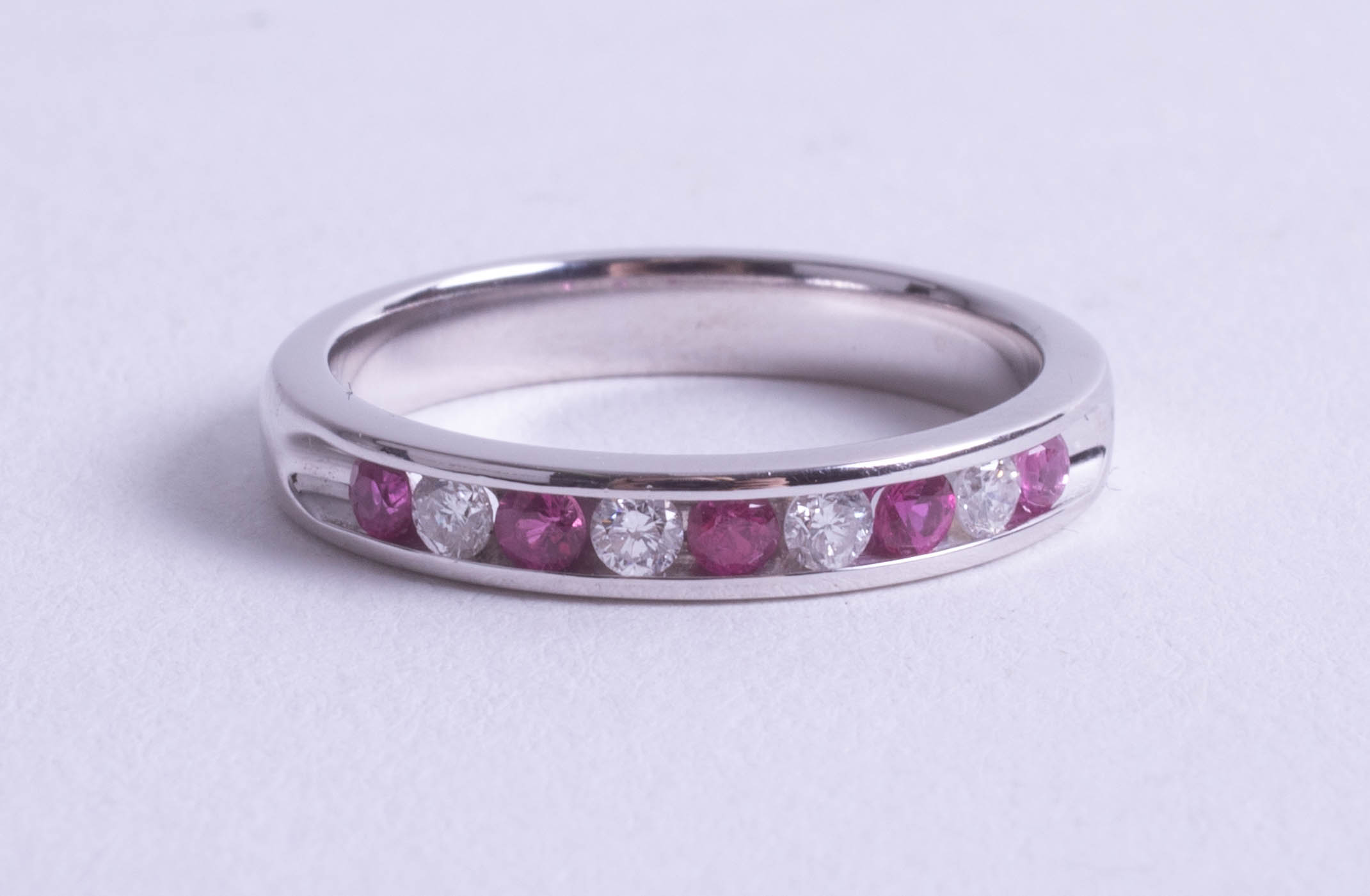 An 18ct white gold ruby and diamond set half band eternity ring, size O.