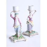 A pair of 18/19th century Meissen candlesticks, modelled as a gallant and his maiden holding baskets