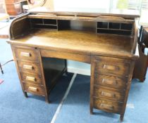 An early 20th century oak roll top desk, the tambour front enclosing various pigeon holes, over a