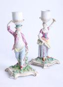 A pair of 18/19th century Meissen candlesticks, modelled as a gallant and his maiden holding baskets