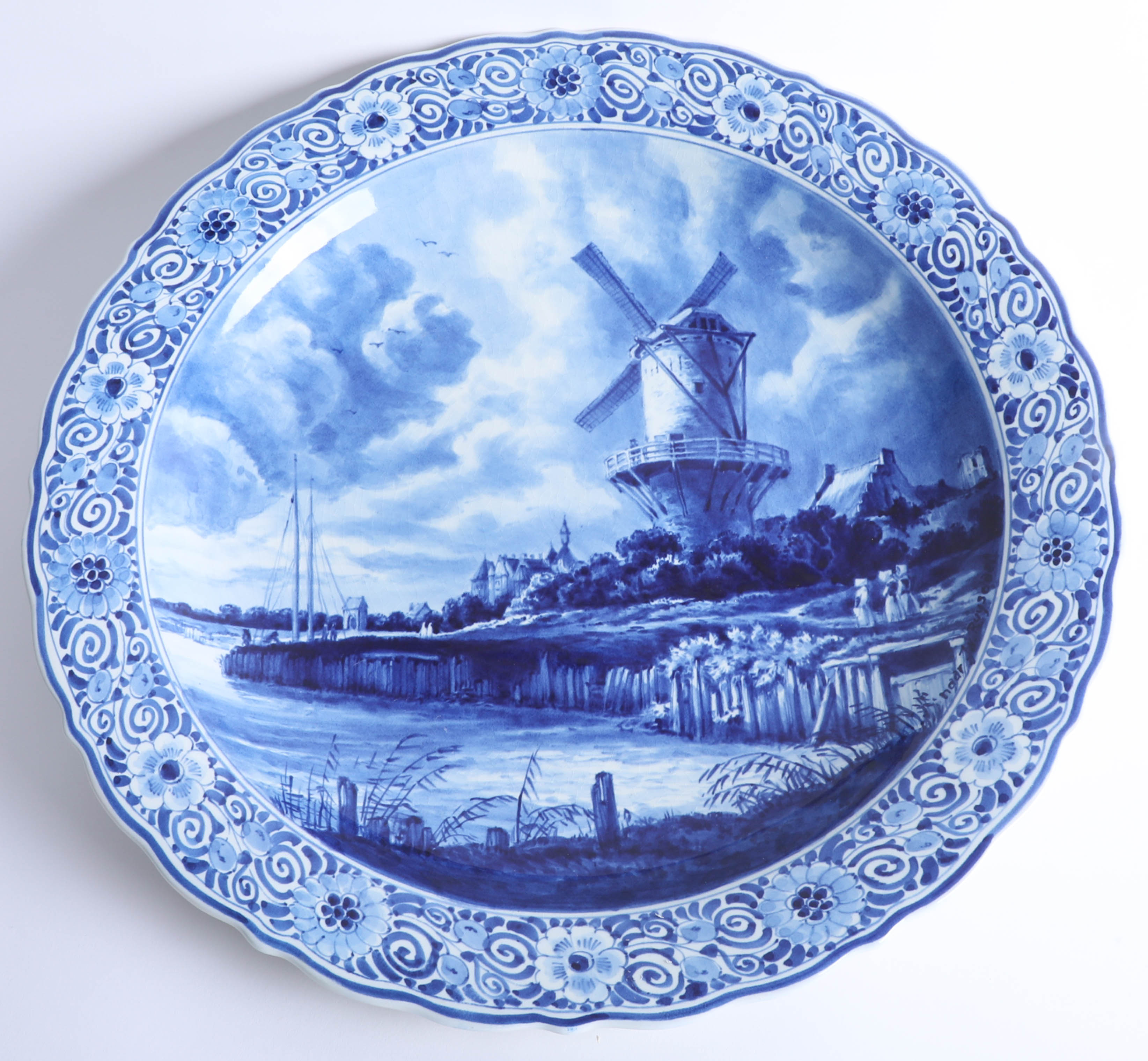 A Delft blue and white charger by Thooft and Labouchere, depicting a windmill on the banks of a