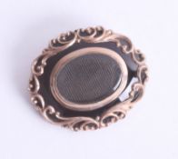 An early Victorian fancy scroll mourning brooch set with black enamel and gold scroll overlay,
