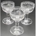 Set of three small wine glasses with drawn stems, the bowls engraved with a border of leaves, c1800,