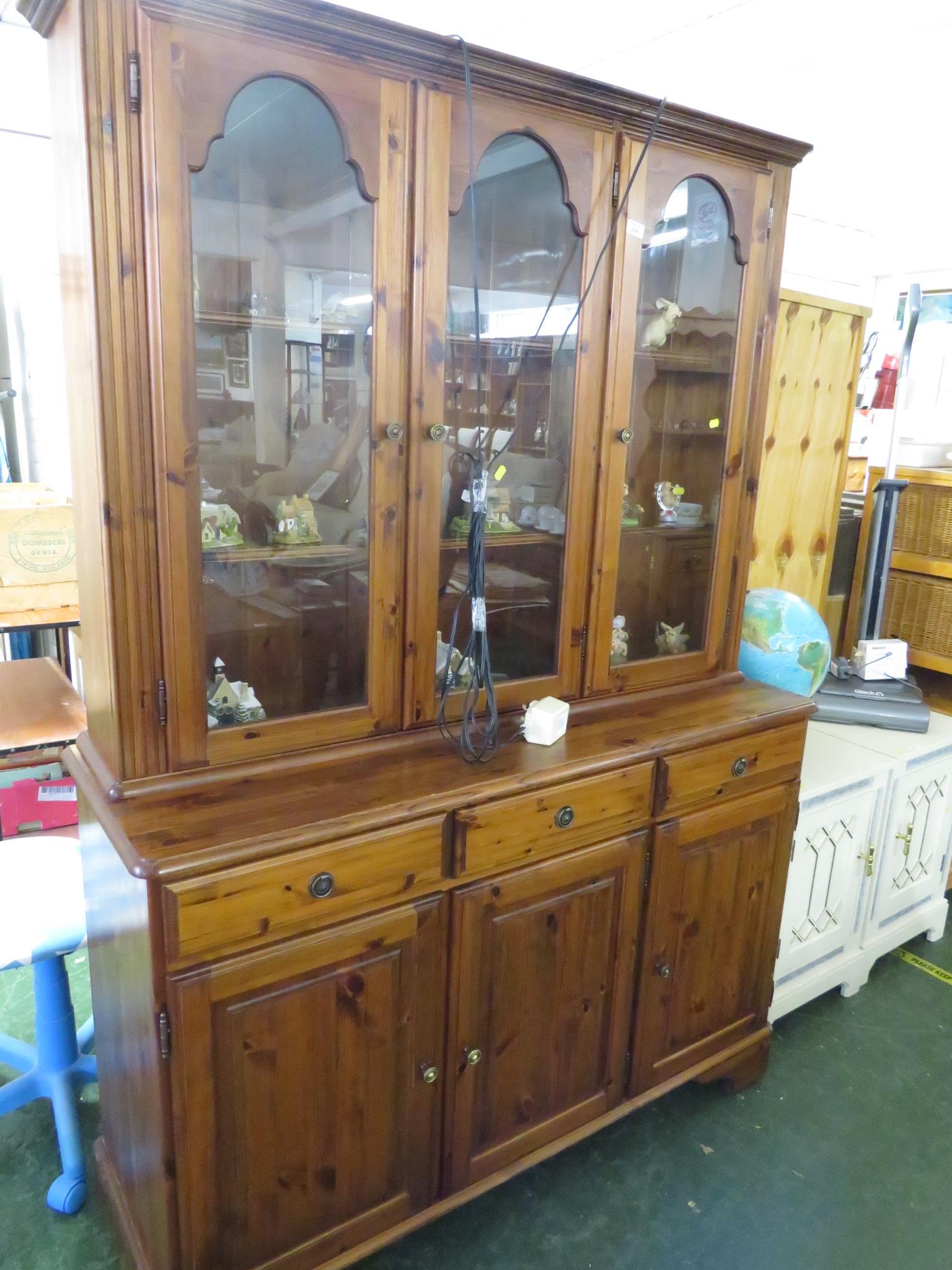 STAINED HONEY PINE GLAZED AND ILLUMINATED DRESSER WITH THREE DRAWERS AND THREE DOORS TO ITS BASE