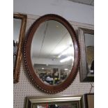 AN OVAL BEVELLED EDGED WALL MIRROR IN A WOODEN FRAME