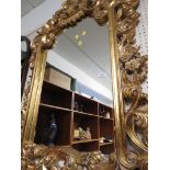 WALL MIRROR IN COMPOSITE GILT EFFECT FRAME HEAVILY MOULDED WITH SCROLLED FOLIAGE