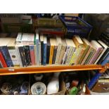 Shelf of paperback books, boxed movie projector, etc