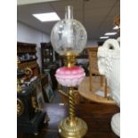A late Victorian brass oil lamp with pink opaline glass font on circular base
