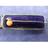 Yellow metal stick pin, with coral bead, in leather case