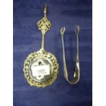 A pair of white metal sugar tongs and tea strainer of pierced designs, probably of foreign