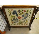 A wood frame glazed needlework fire screen depicting a floral scene and hung on barley twist legs