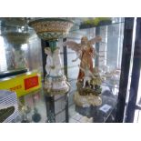 A porcelain figure depicting an angel standing over a small boy and girl with a dish on a pedestal