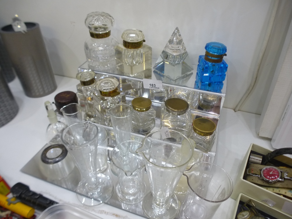 A quantity of cut glass ink wells, alongside a quantity of glass measures, etc