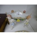 A pair of Coalport plates and a Dresden bon-bon dish, supported by cherubs