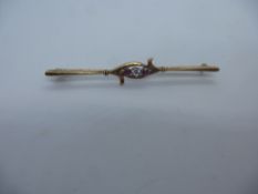 Unmarked yellow metal bar brooch with central diamond flanked with rubies, unmarked, pin slightly