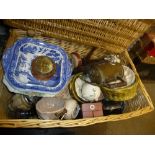 A large wicker basket full of sundry items to include vegetable serving dishes, vintage brass