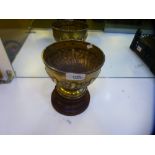 A large heavy silver Edwardian trophy cup on a wooden stand. Cup decorated with embossed foliate