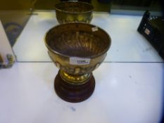 A large heavy silver Edwardian trophy cup on a wooden stand. Cup decorated with embossed foliate