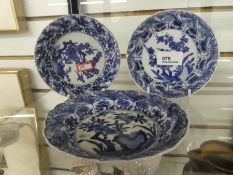 Three Chinese blue and white dishes decorated with trees and flowers.