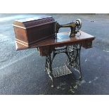 A Singer sewing machine on walnut table with drop-leaf, having three frieze drawers, on cast iron