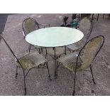 A circular garden table with four chairs, the bevelled plate glass top on wrought iron base, the