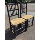 A pair of ebonised oak chairs with rush seats, the backs with two rows of spindles, raised on turned