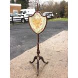 A Victorian mahogany firescreen, the shield shaped glazed floral crewelwork panel on adjustable