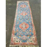 An oriental wool runner woven with three scalloped floral medallions on blue field with entwined