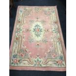 A Chinese thick pile wool rug woven with oval scalloped flower medallion in pink field framed by