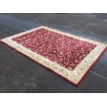 A rectangular floral woven rug, the maroon field with scrolled leaf design framed by ivory frieze