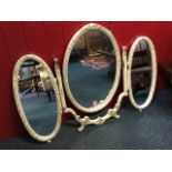 An oval painted dressing table mirror, the central easel mounted plate flanked by two hinged
