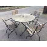 A circular Kewdog teak garden table with four armchairs, the table with radiating slats on folding