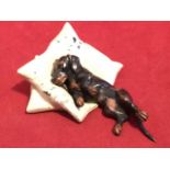 A cold painted bronze cast as a dachshund lying on pillows - impressed Geschutzt. (1.25in)