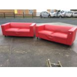 A pair of red leather sofas with rectangular platform arms and cushion seats, raised on tubular