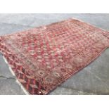 An antique Afghan rug woven with rows of oval geometric medallions and crosses on madder field,