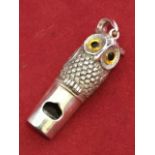 A sterling silver owl whistle, the cast bird having applied yellow glass eyes, with ring mount to