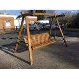 A swinging garden seat, the sturdy “A” frame supporting a slatted bench with platform arms and