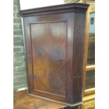 An early nineteenth century mahogany corner cabinet, with moulded cornice above a panelled door
