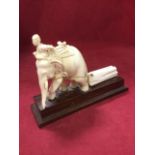 A carved ivory elephant group with mounted saddled animal pulling log, on rectangular rosewood