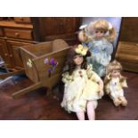 Three porcelain girl dolls with painted faces in lace trimmed dresses; a toy wheelbarrow; an