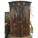 A nineteenth century bowfronted mahogany corner cabinet, with moulded cornice above frieze inlaid