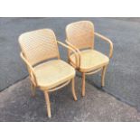 A pair of beech bentwood armchairs with rounded backs and arms having cane panels, raised on