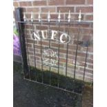 A wrought iron side gate hinged on wood post, having spear finials above NUFC arched label applied