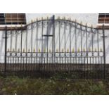 A pair of wrought iron driveway gates with tubular poles in arched frames with fleur-de-lils finials