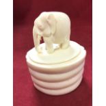 A carved ivory box & cover of oval ribbed form, the lid mounted with a finely carved elephant. (4.