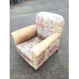 An Edwardian upholstered armchair with rounded padded back above a sprung seat, raised on square