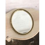 An oval bevelled mirror in leaf moulded scrolled gilt frame. (20in x 26in)