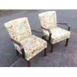 A pair of oak armchairs with floral tapestry upholstery having rounded bentwood arms and loose