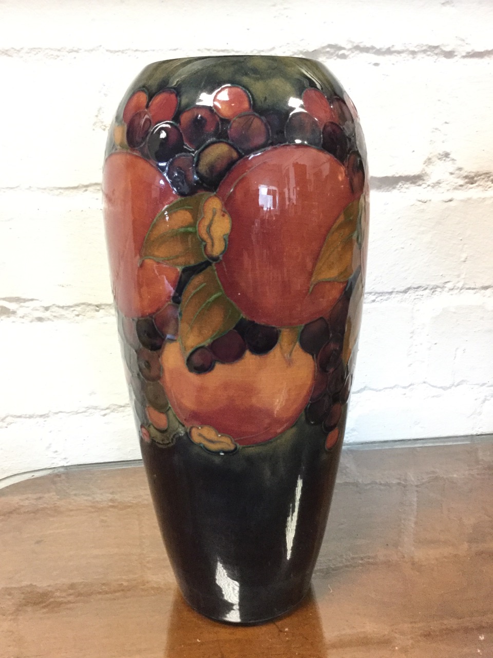 A tall tapering Moorcroft vase embossed with tube-lined vines and pomegranates on dark glazed ground